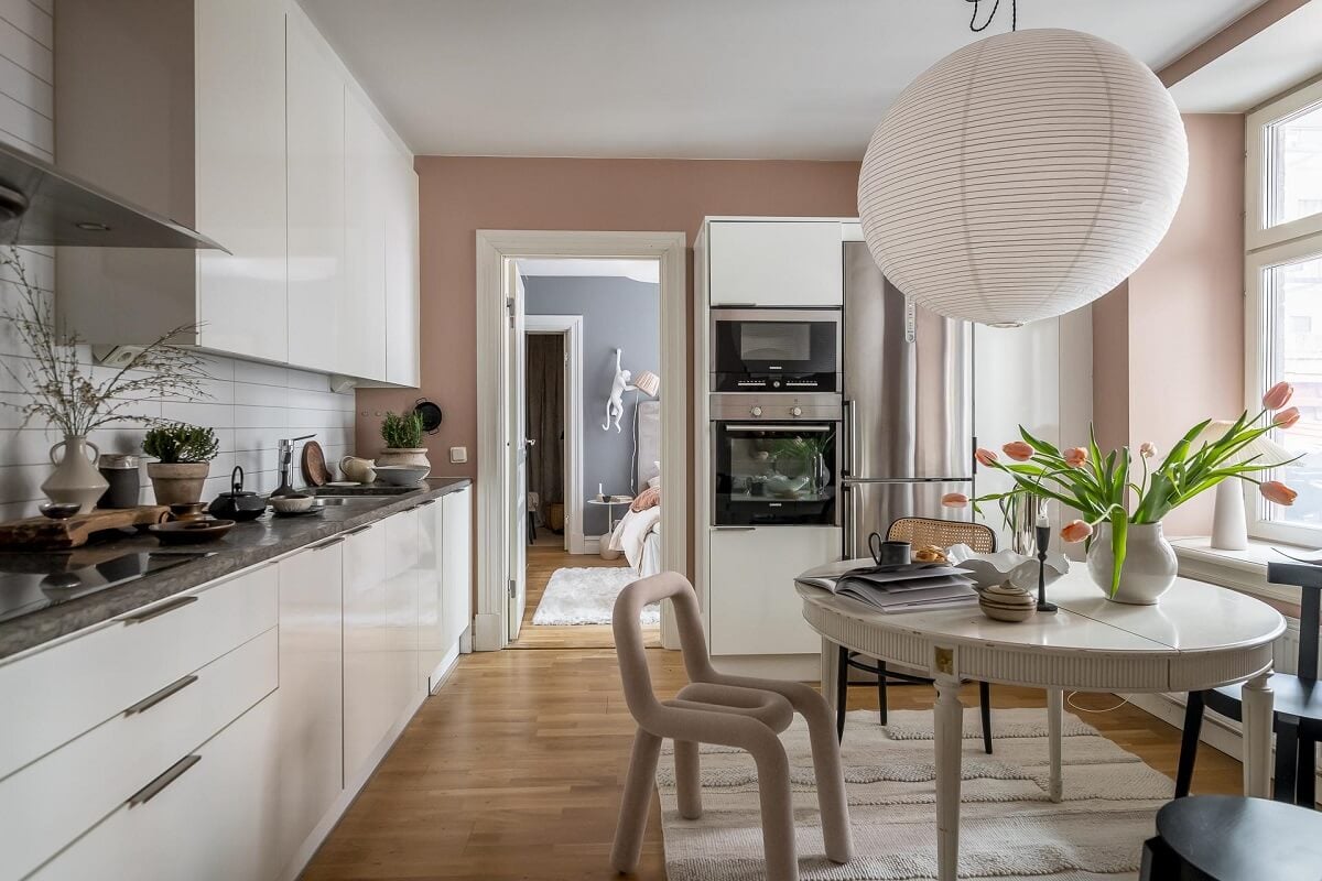 Layered Textiles and Dusty Colors in a Nordic Apartment 9 kitchen-white-cabinets-pink-walls-round-dining-table-nordroom