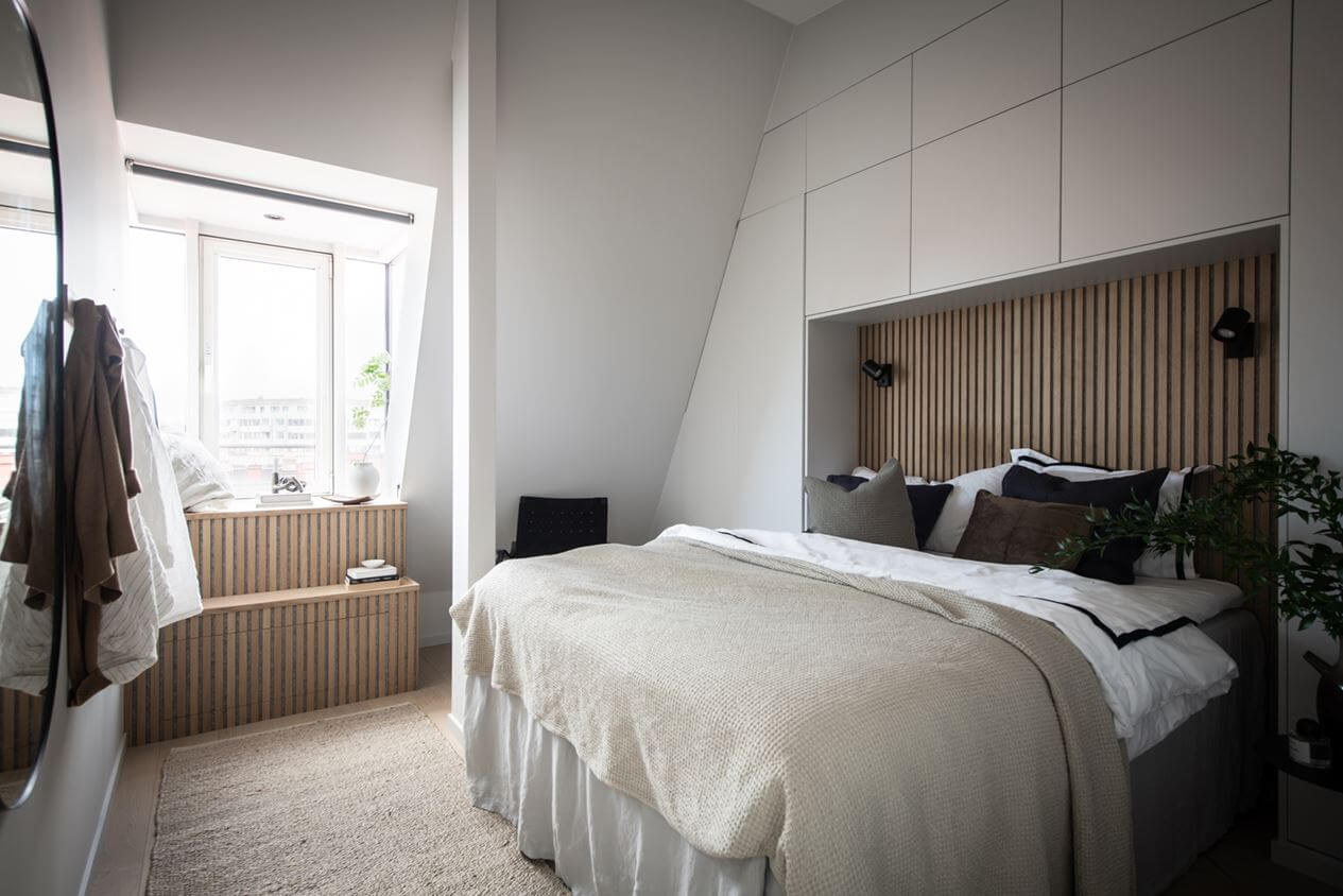A Stylish Scandinavian Attic Apartment 11 master-bedroom-attic-slanted-ceiling-wood-slat-accent-wall-built-in-cabinets-nordroom