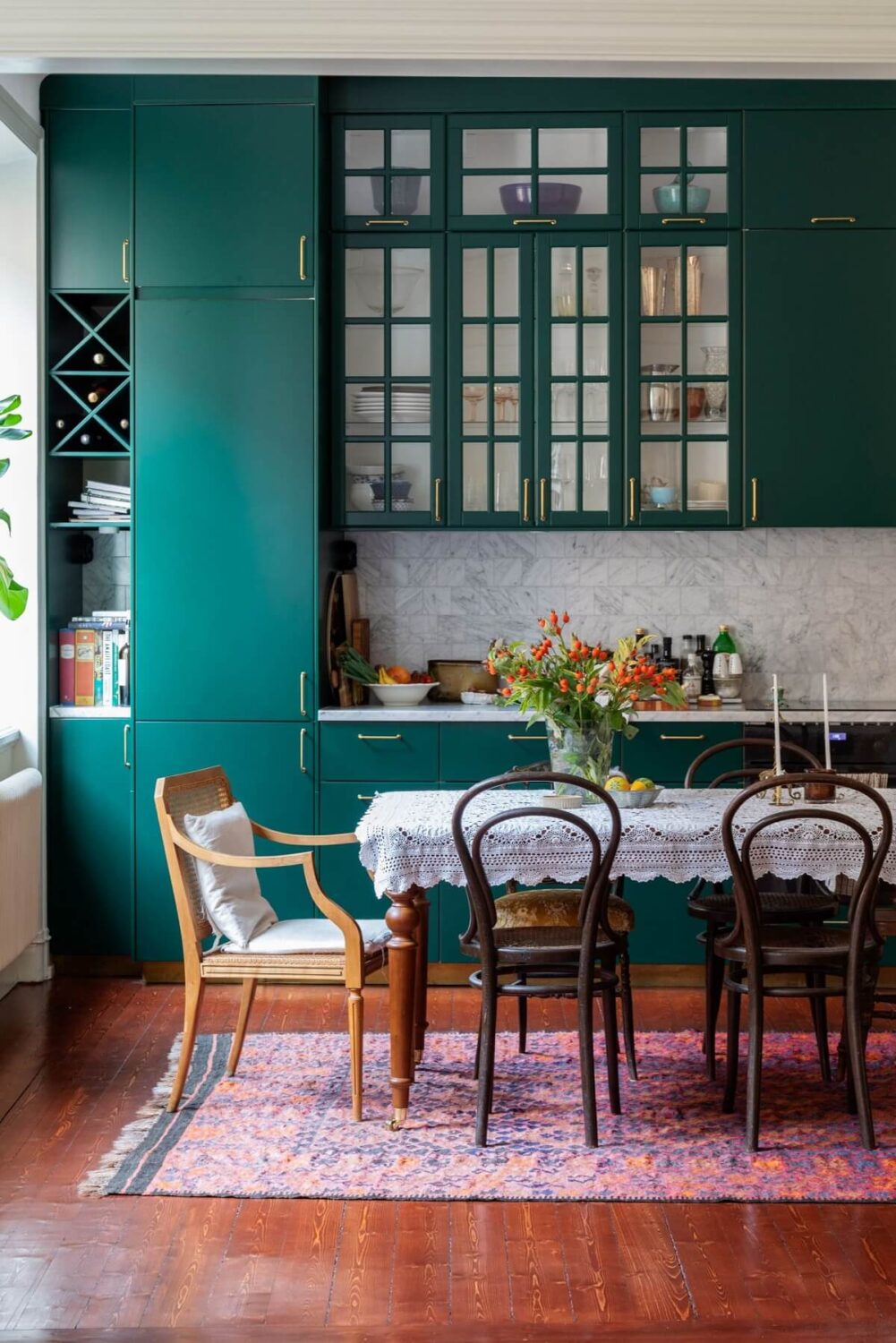 A Cozy Swedish Apartment with a Green Kitchen 7 green kitchen with dining table vintage chairs mahogany floor pink rug