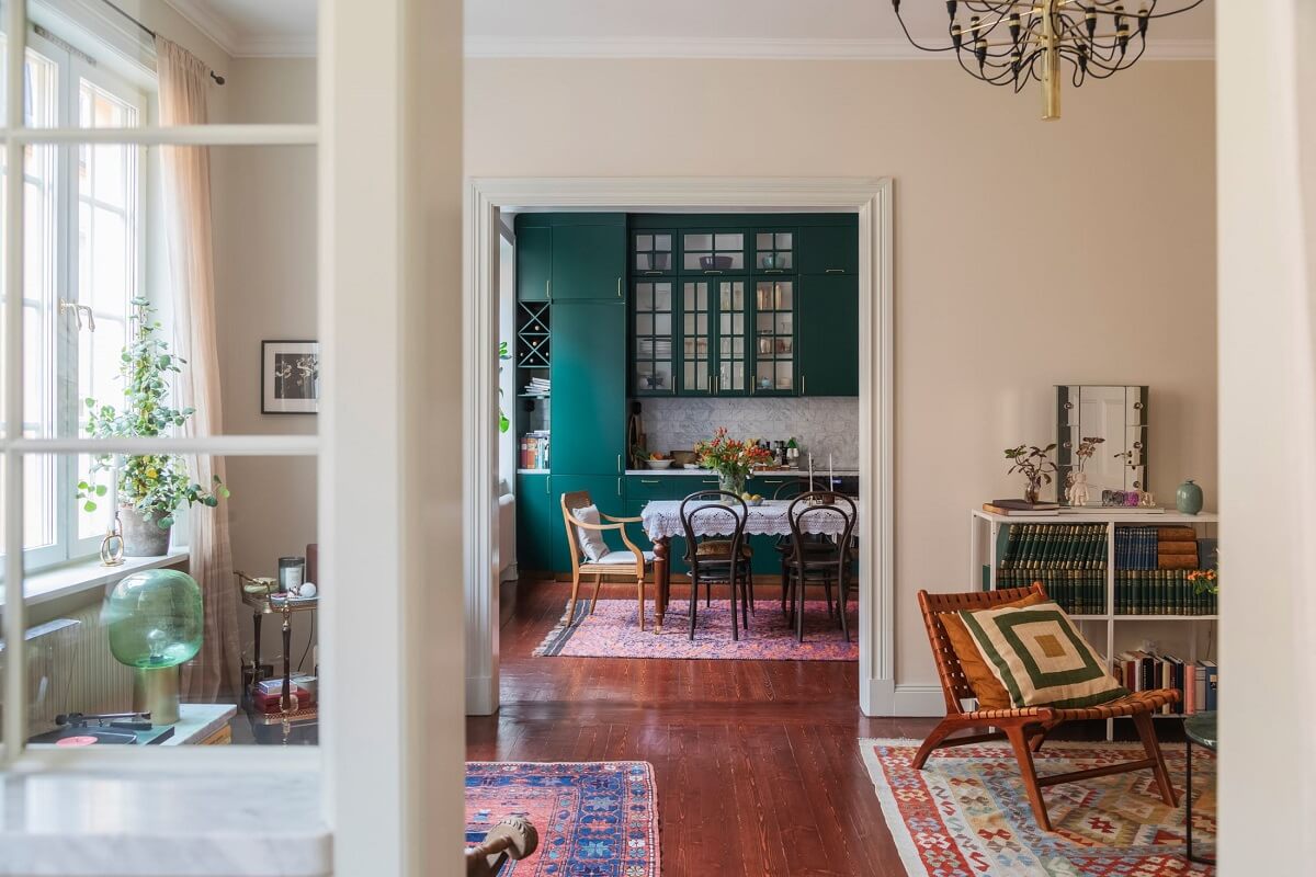 A Cozy Swedish Apartment with a Green Kitchen 15 view into living room kitchen green cabinets mahogany stained floor nordroom