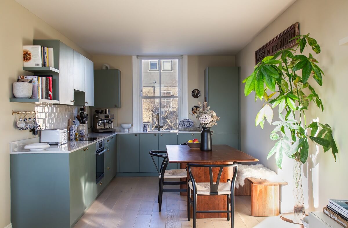 An Exposed Brick Wall in a London Duplex Apartment 9 kitchen with sage green cabinets and wooden dining table