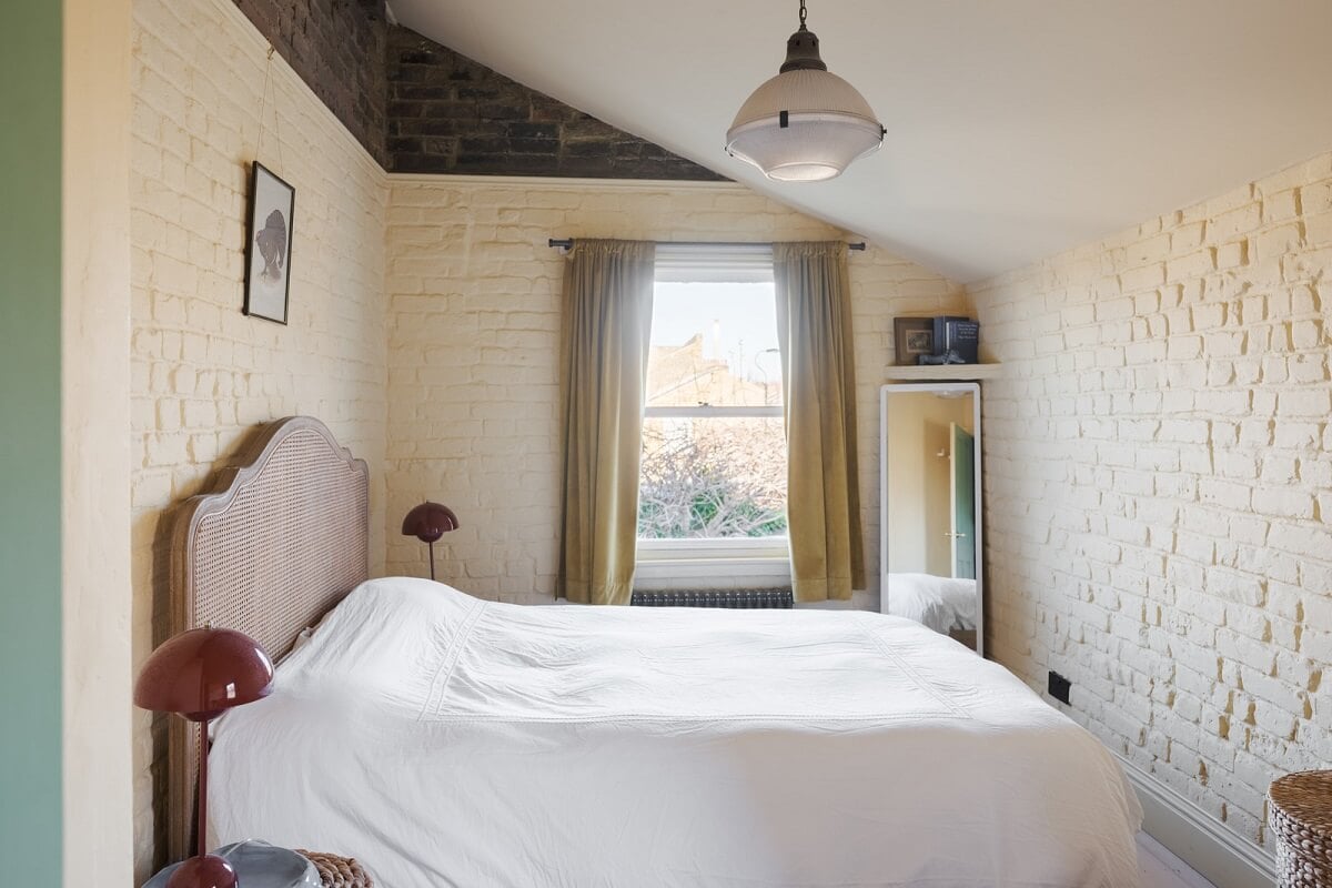 A London Home with Green Color Accents 13 bedroom with slanted ceiling and painted brick wall