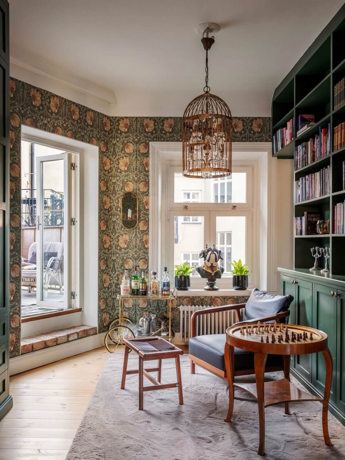 A Classic Swedish Apartment Decorated in Green and Pink Tones 11 reading room with william morris wallpaper and green bookcases