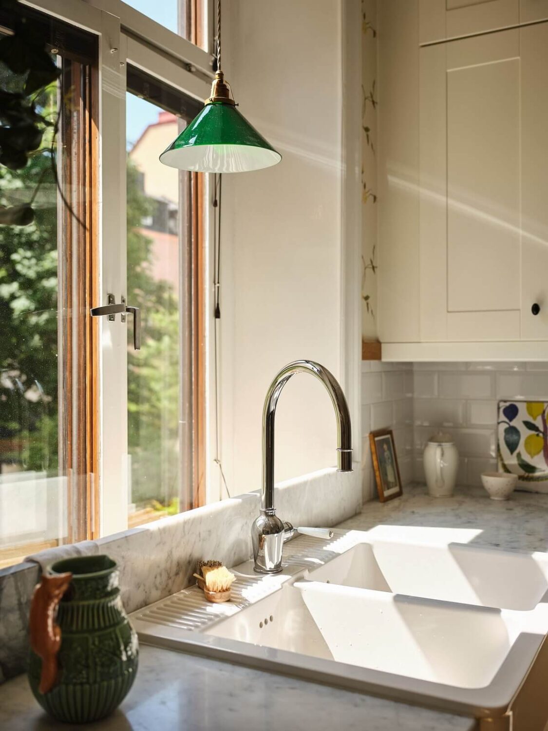 A Classic Stockholm Apartment with Floral Wallpaper 15 kitchen sink under window with green pendant nordroom