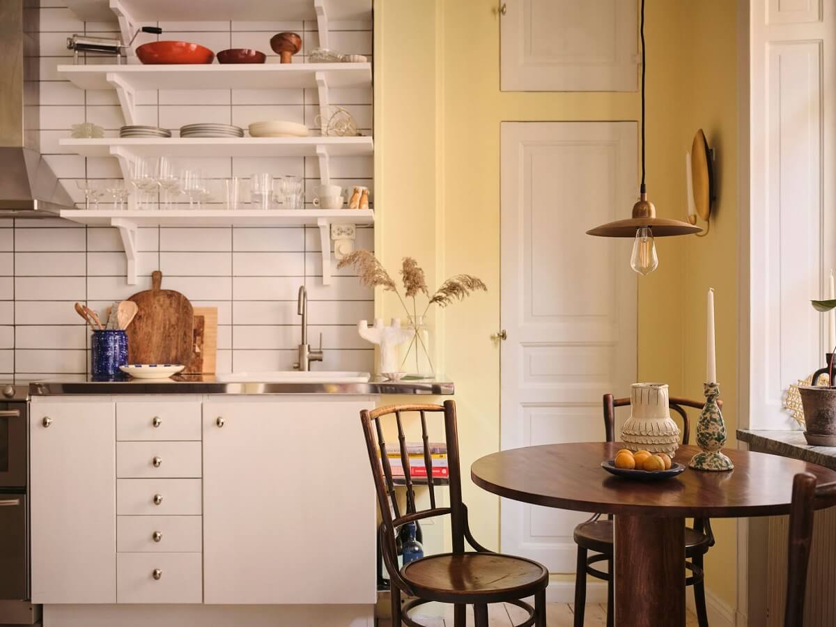 A Small Apartment with Calm Brown, Green, and Yellow Walls 6 kitchen with white cabinets yellow walls and round wooden table nordroom