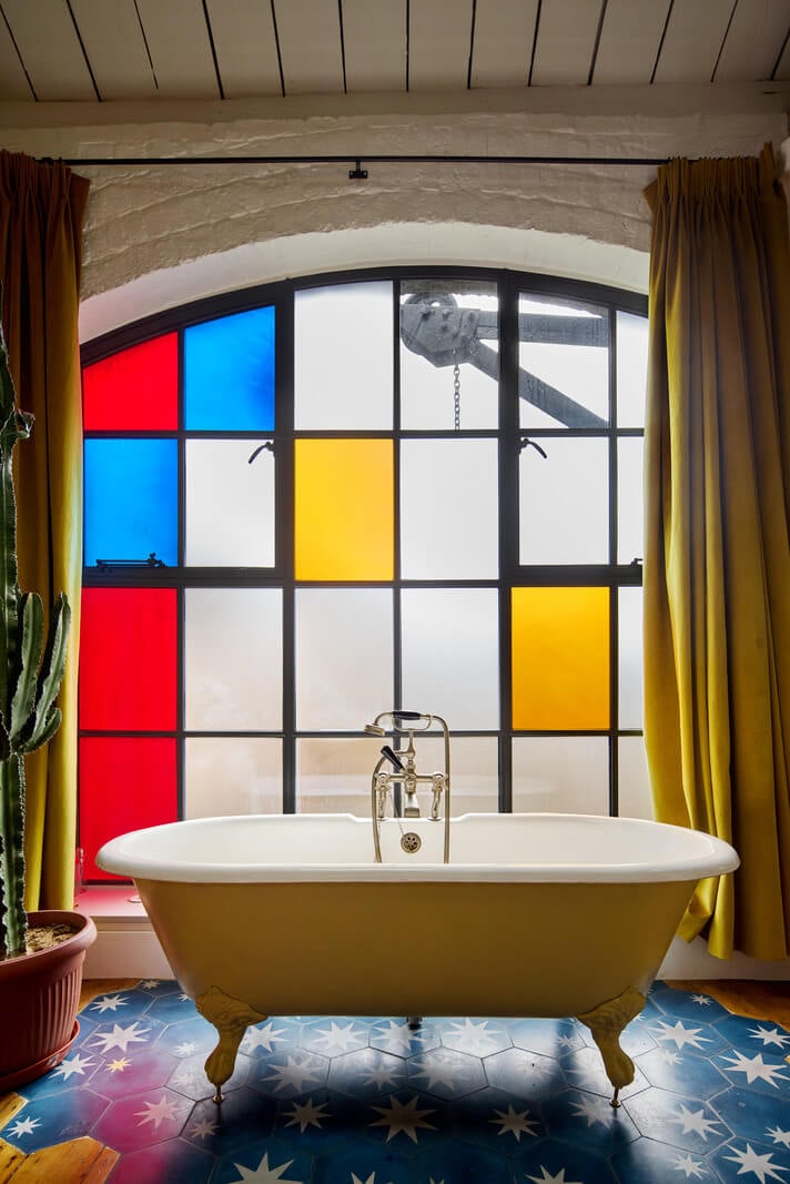 An Industrial and Colorful Warehouse Conversion in London 16 bathroom with freestanding yellow bath and stained glass window nordroom
