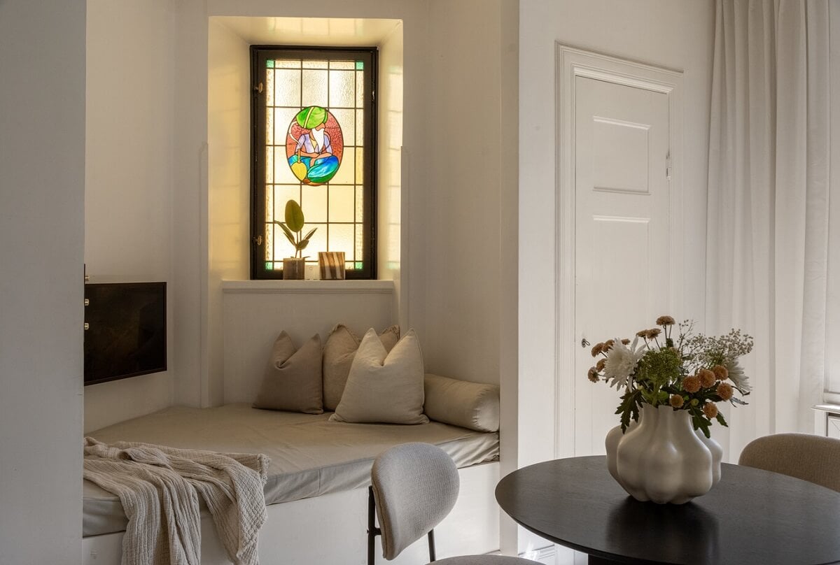A Tiny Minimalistic Apartment in Stockholm 6 living room with angled built in sofa and stained glass window