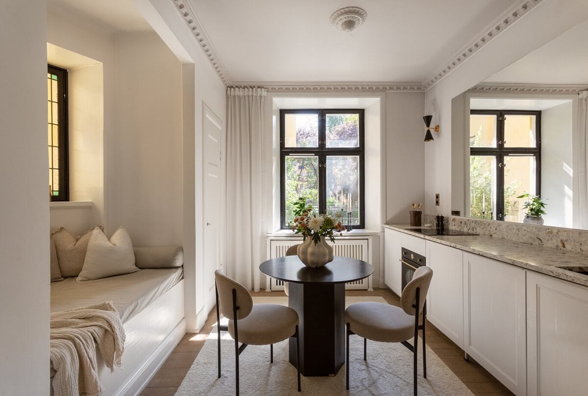 A Tiny Minimalistic Apartment in Stockholm 1 small living room wih built in sofa in niche round table and kitchen with large mirror