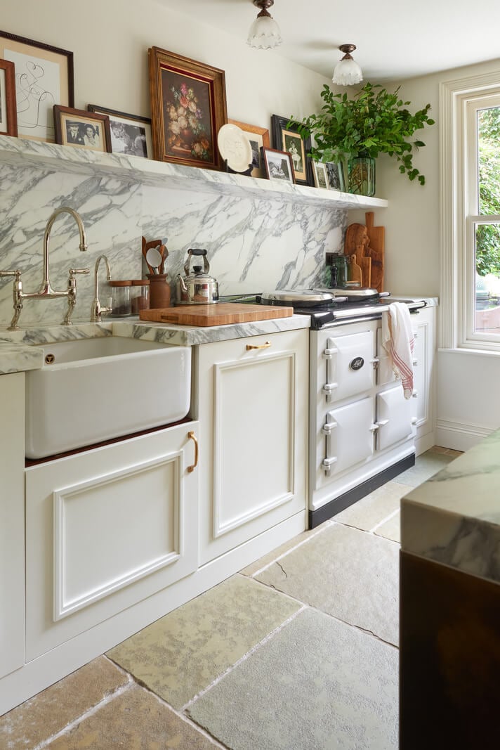 A Luxurious Two-Bedroom Maisonette in Primrose Hill 8 white kitchen with butler sink aga stone marble backsplash and shelf with vintage art