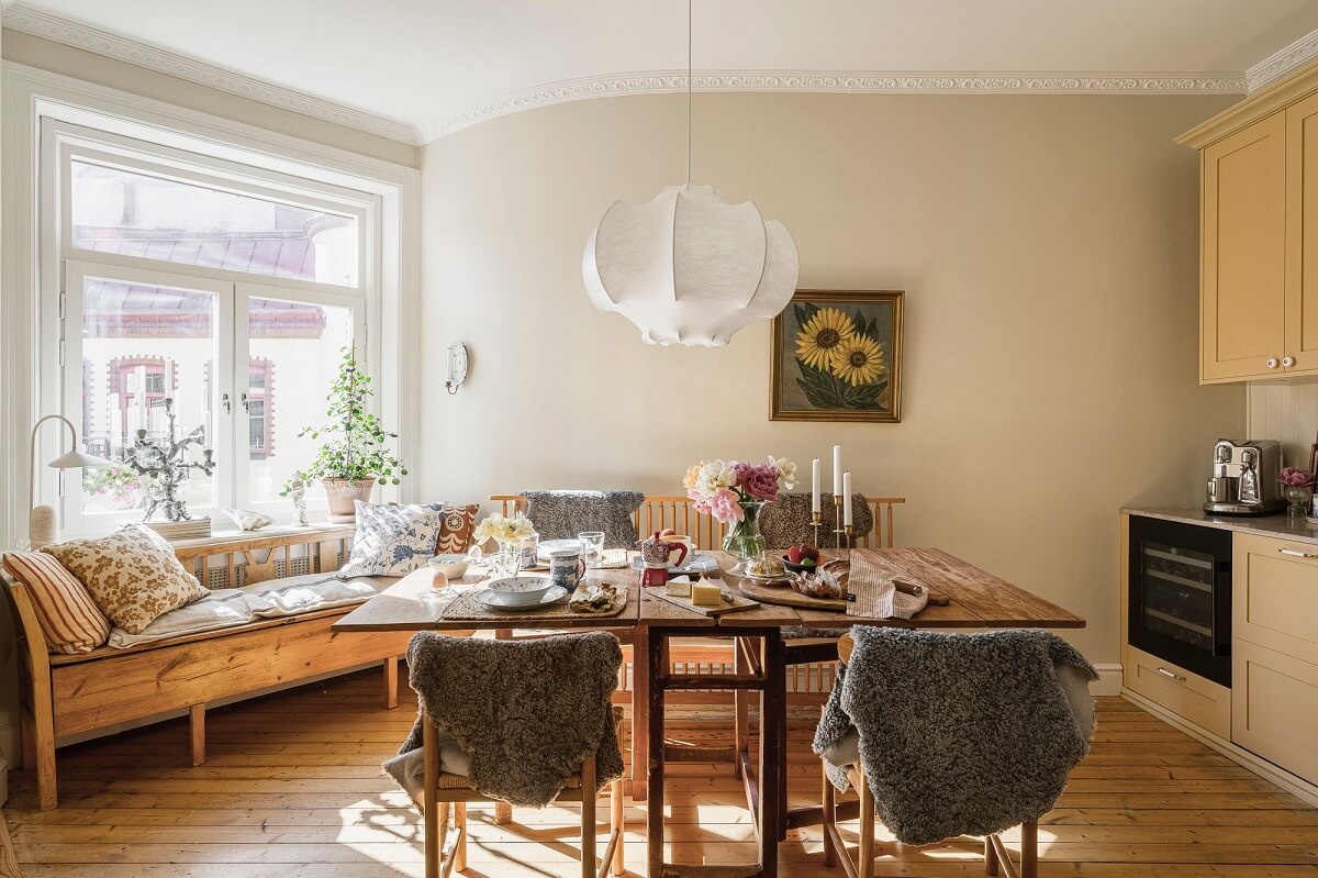 Hannes Mauritzson's Warm Yellow Hygge Apartment in Sweden 27 butter yellow kitchen with wooden table and window seat