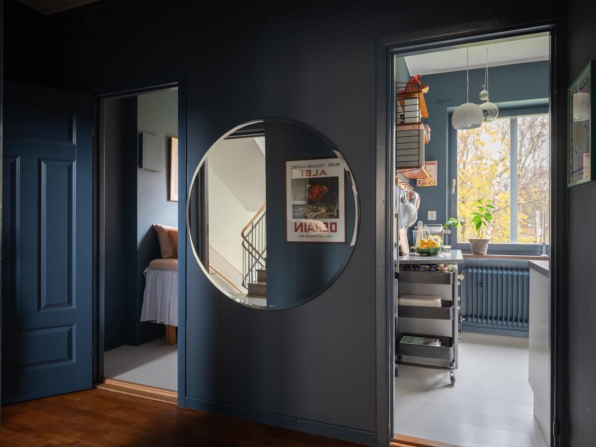 A Small Swedish Apartment with Dark Blue Walls 10 blue hall with large round mirror