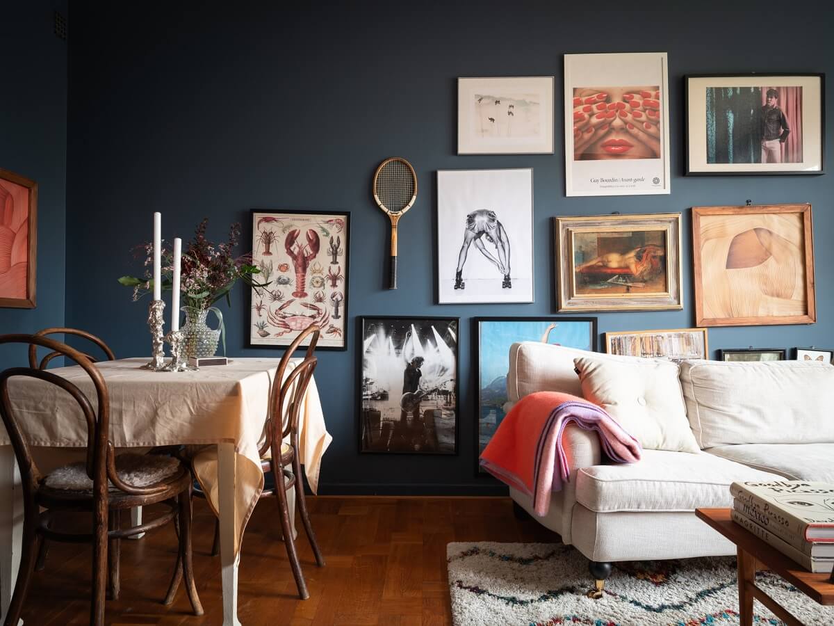 A Small Swedish Apartment with Dark Blue Walls 4 blue living room with dining table and gallery wall