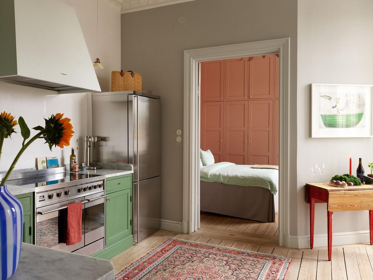 A Colorful Turn-of-the-Century Family Apartment in Stockholm 19 green kitchen with adjacent pink bedroom
