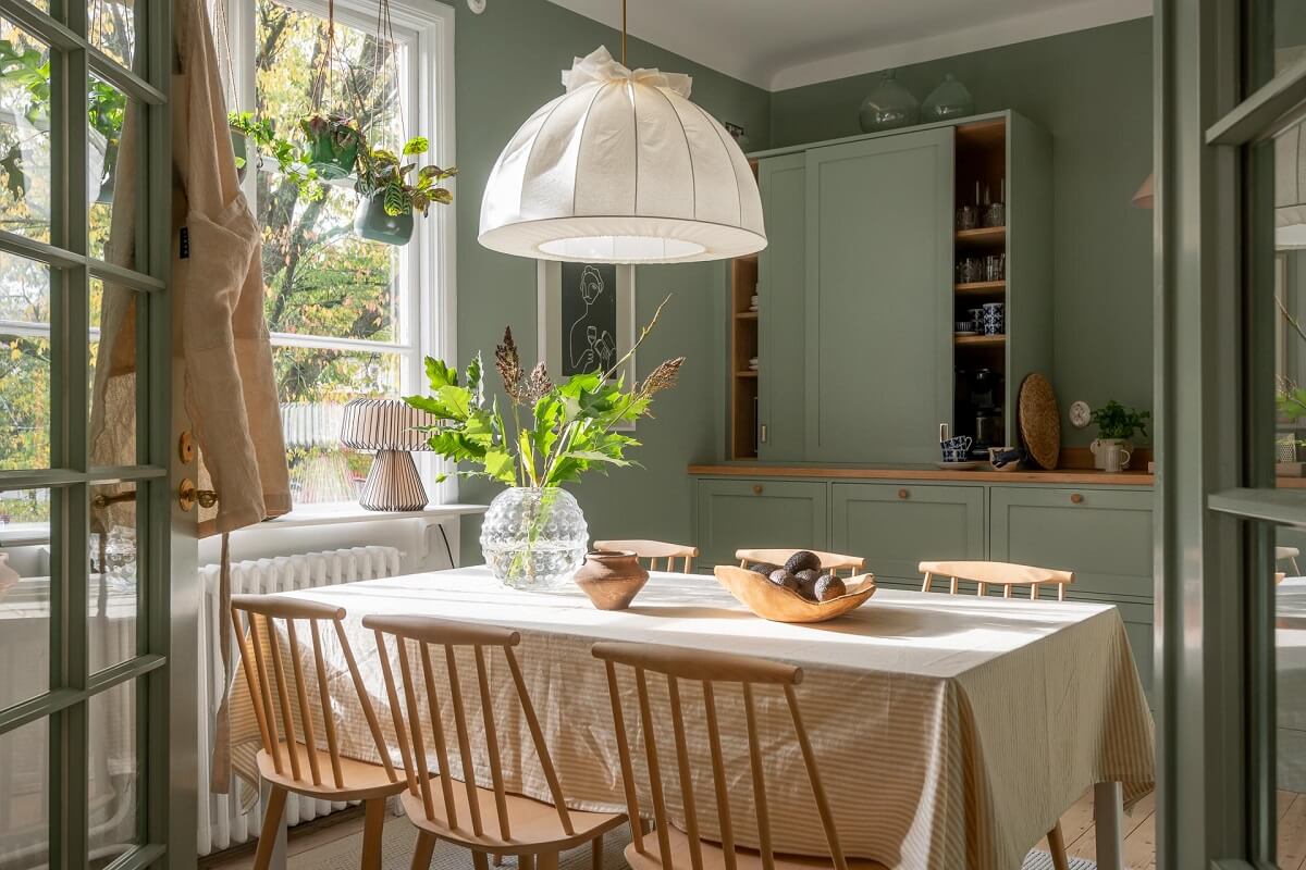 A Swedish Apartment Painted in Calm Beige, Green, and Pink Tones 10 green kitchen with dining table and plants