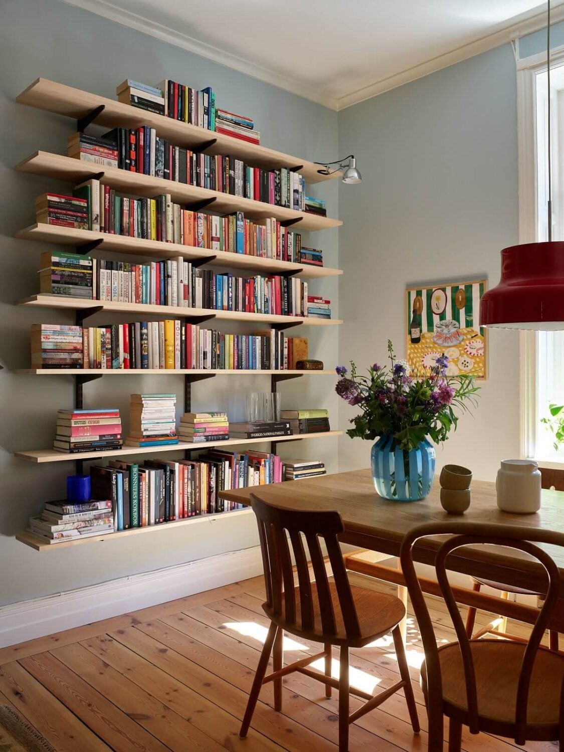 A Light Turn-of-the-Century Apartment with a Cheerful Color Palette 3 light blue walls living room with wooden dining table and bookshelves