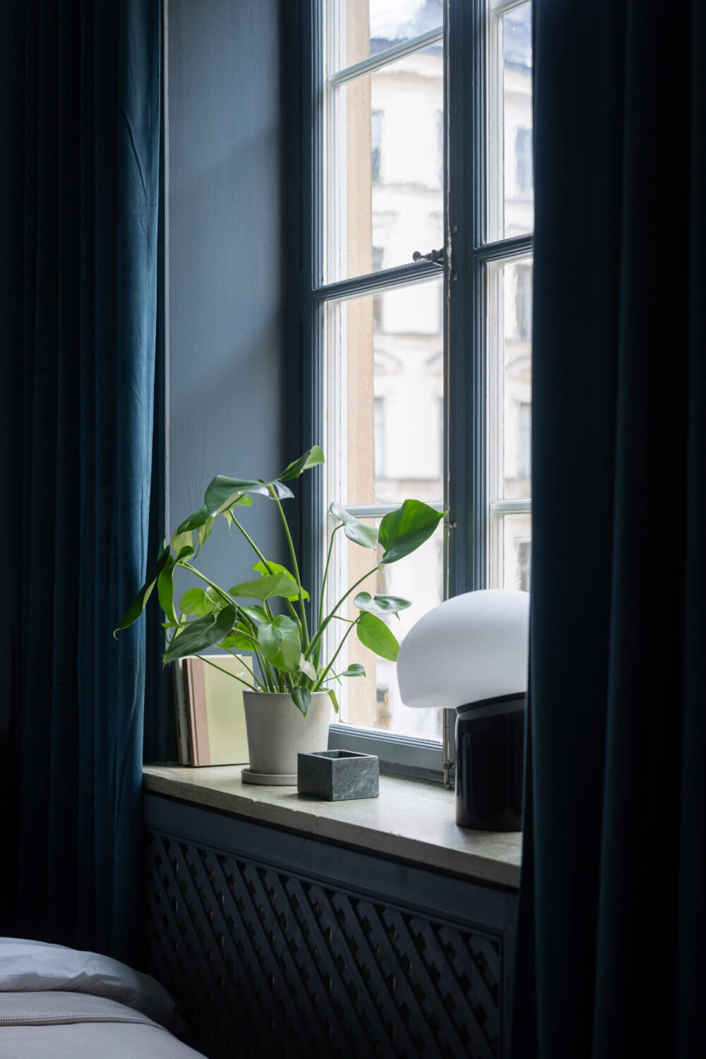 A Moody Color Palette in a Stylish One-Bedroom Apartment in Stockholm 12 bedroom window with blue velvet curtains