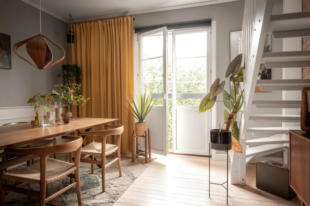 A Swedish Attic Apartment with Exposed Brick and Yellow Color Accents 2 gray dining room large wooden table ochre yellow curtains
