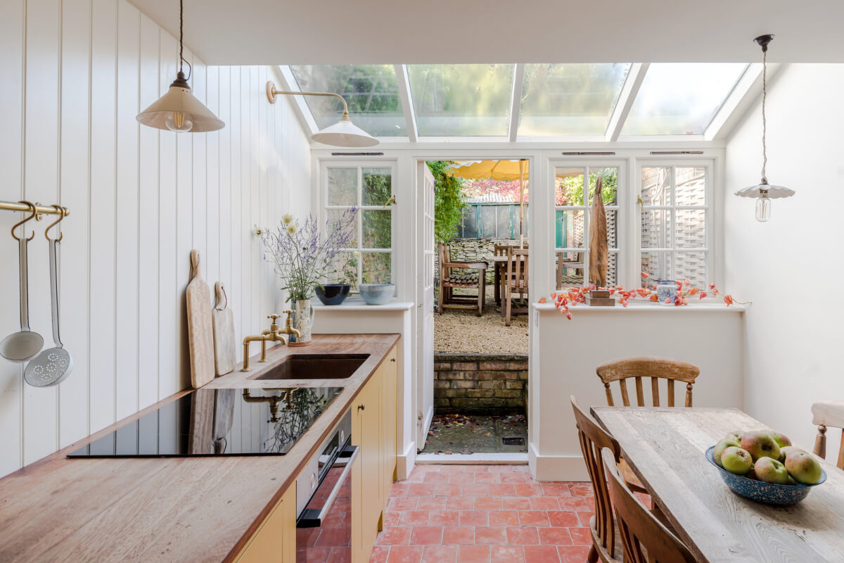 A Carefully Selected Color Palette in an 18th-Century English Cottage 7 kitchen with ochre cabinets stone floor wooden table and tongue and groove paneling