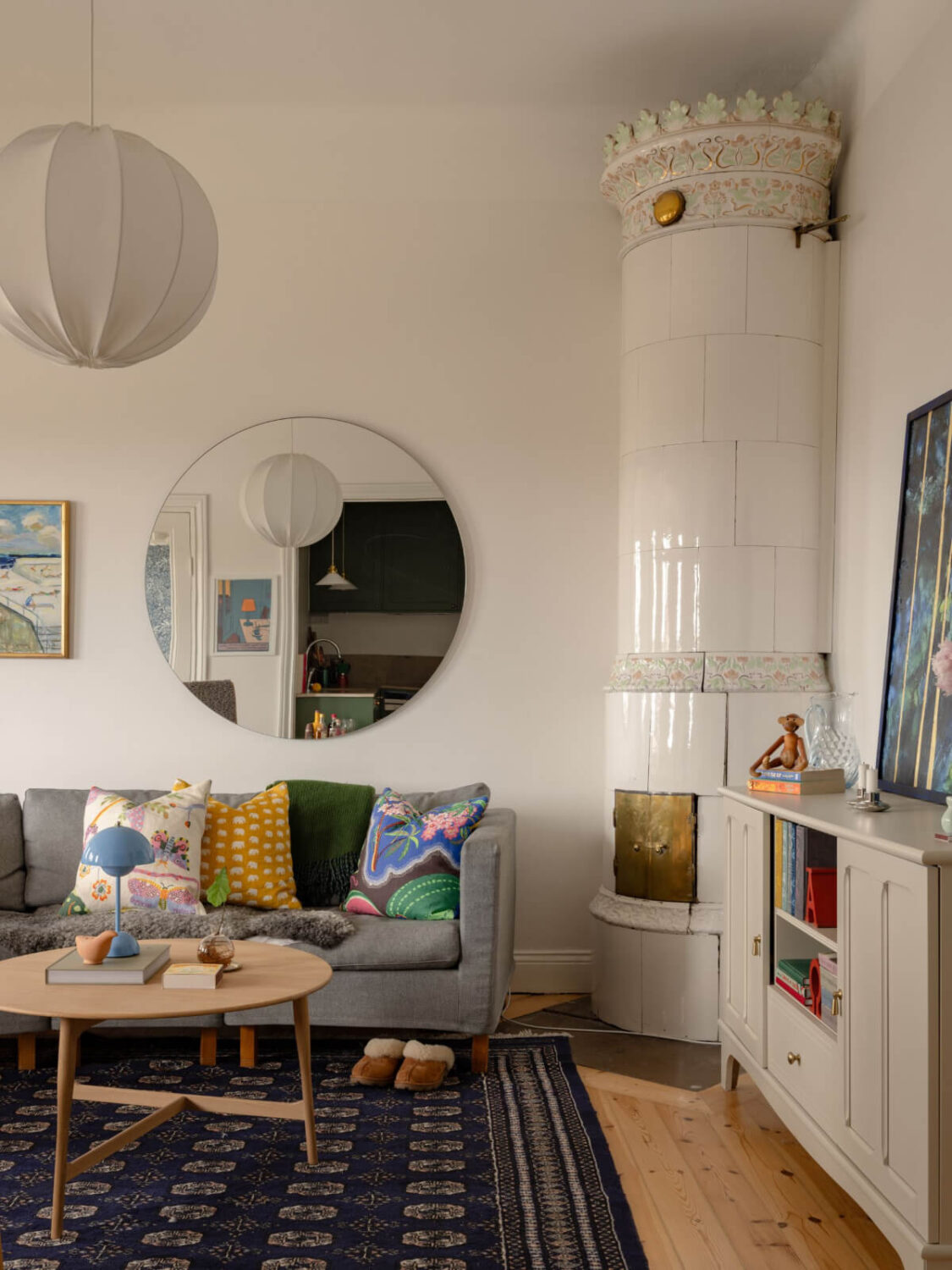 A Small Apartment with High Ceilings and a Large Bay Window 4 living room wooden floor blue rug fireplace round mirror