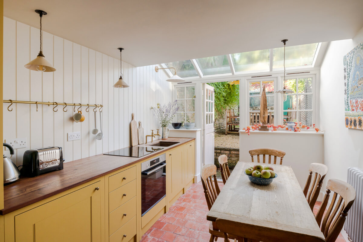 Best of 2025: Kitchens 42 ochre yellow kitchen with brass fittings stone floor and wooden table