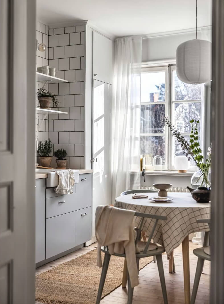 A Beige Studio Apartment with a Bright Kitchen 8 scandi kitchen gray cabinets white tiles round table nordroom