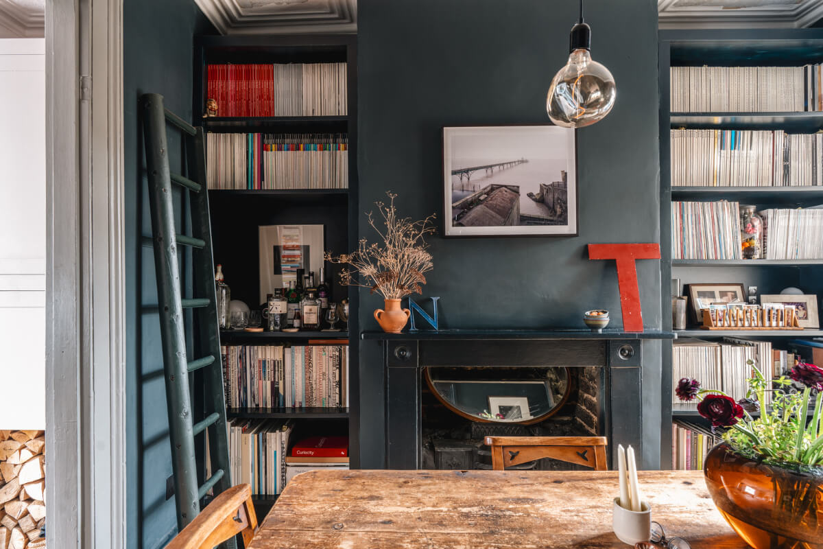 A Cozy Victorian Home Painted in Moody Blue and Gray Tones 6 dark blue dining room fireplace bookshelves rustic wooden table