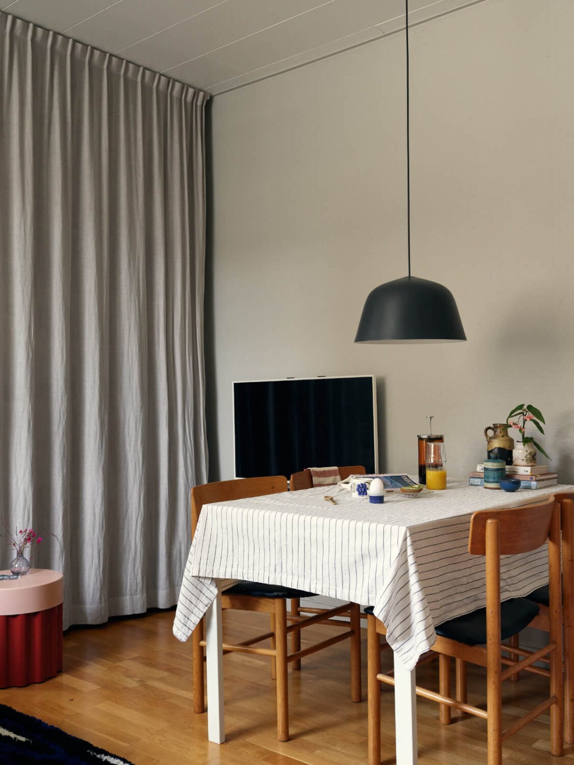 A Tiny Apartment with a Semi-Open Floorplan and a Pink Kitchen 5 dining table storage behind curtains