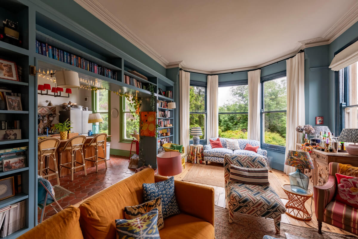 A Colorful Eclectic Victorian Maisonette Home in England 2 open-plan living room kitchen blue walls bookshelves bay window