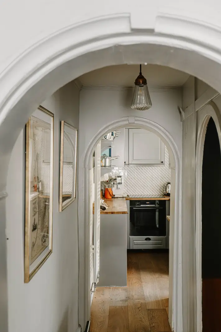 A 17th-Century Home with Original Elements in an English Seaside Town 8 arched doorway into small gray kitchen