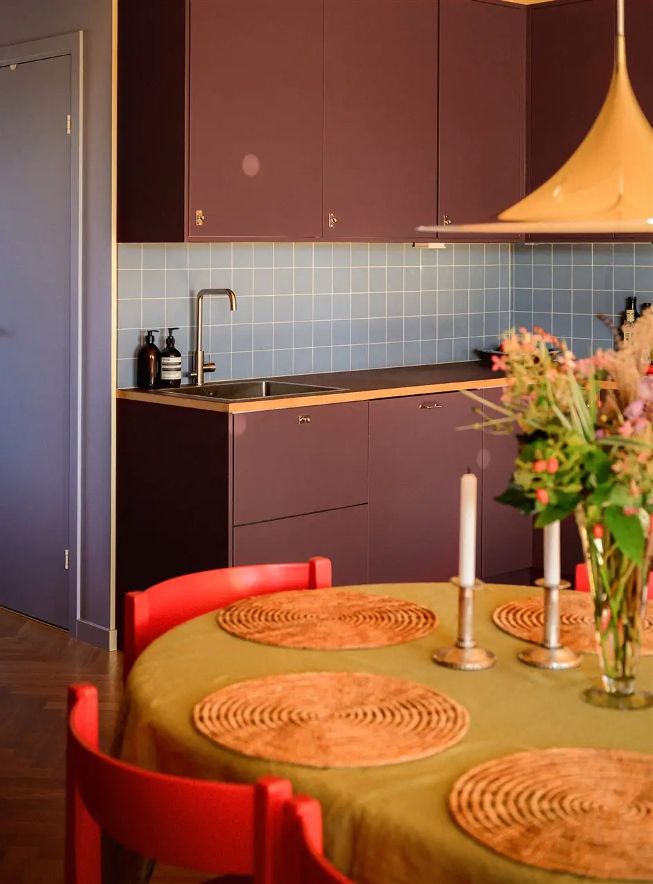 A Colorful Stockholm Family Apartment with Views of the Lake 12 kitchen plum colored cabinets dining table with red chairs nordroom